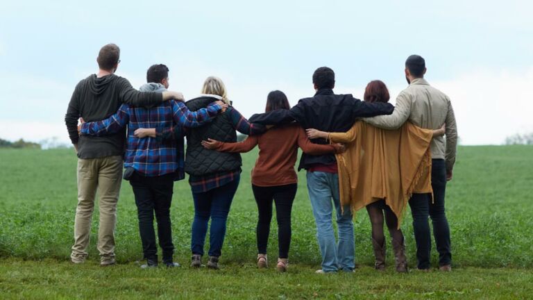 Group of friends outside looking out on a field with arms around each other.